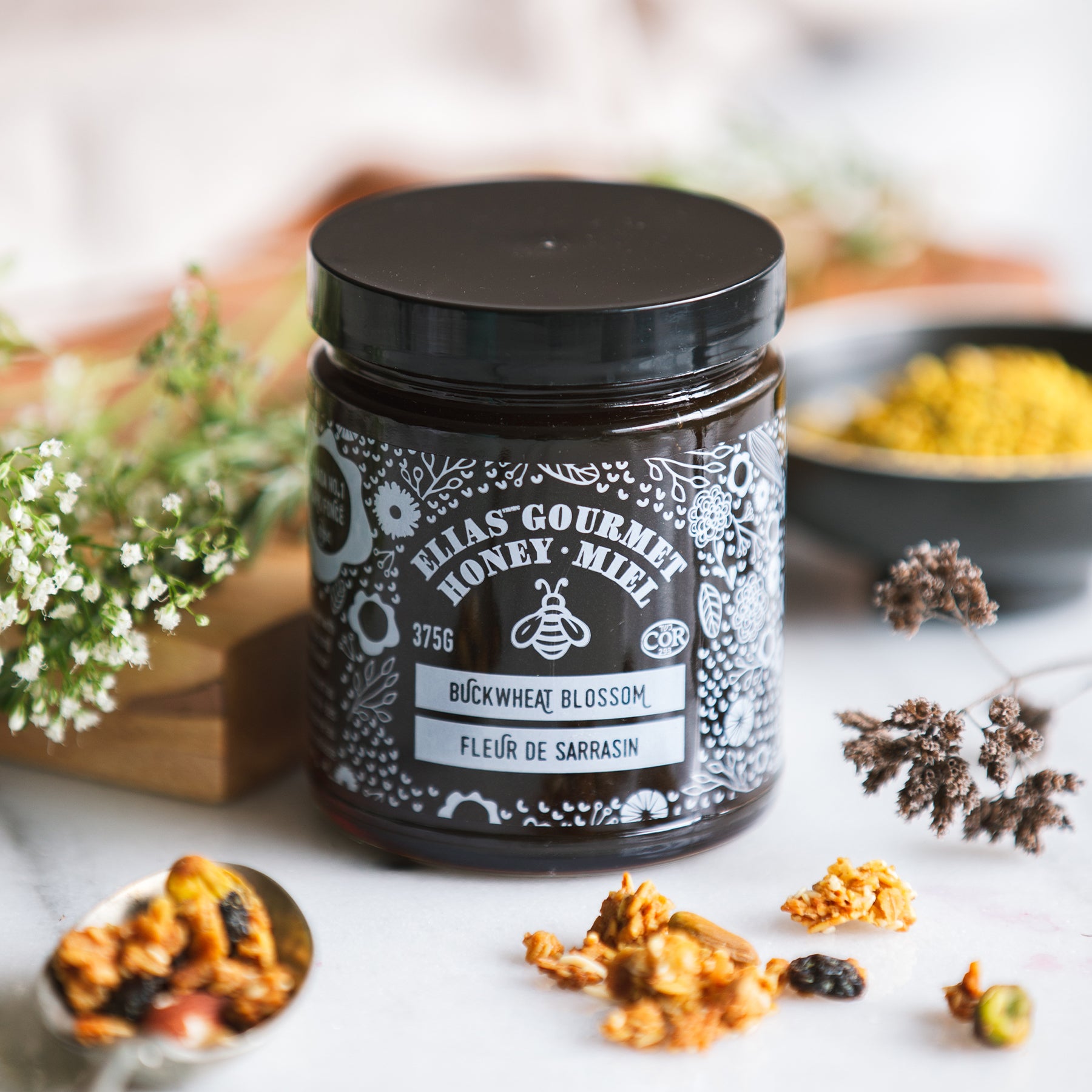 Image of Elias Gourmet Buckwheat Blossom Honey in front of flowers