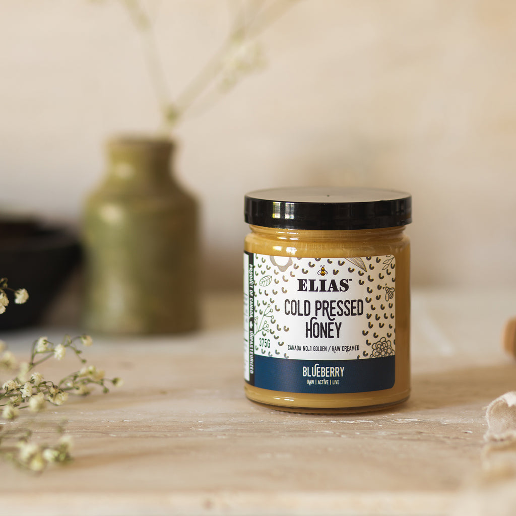Image of Elias Canadian Blueberry Cold Pressed Honey in front of a vase and flowers