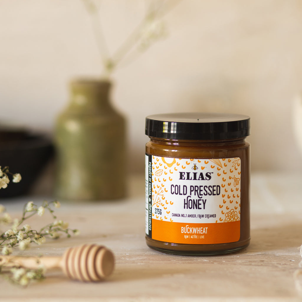 Image of Elias Canadian Cold Pressed Pure Buckwheat Honey in front of a vase and flowers