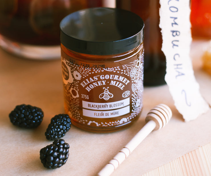 Elias Honey - Blackberry Blossom Honey beside blackberries, with the text ‘gourmet honey’