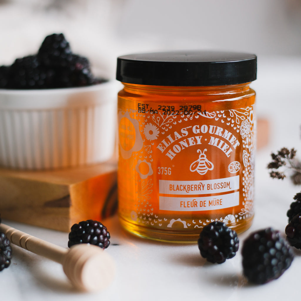 Image of Elias Gourmet Blackberry Blossom Honey in front of blackberries